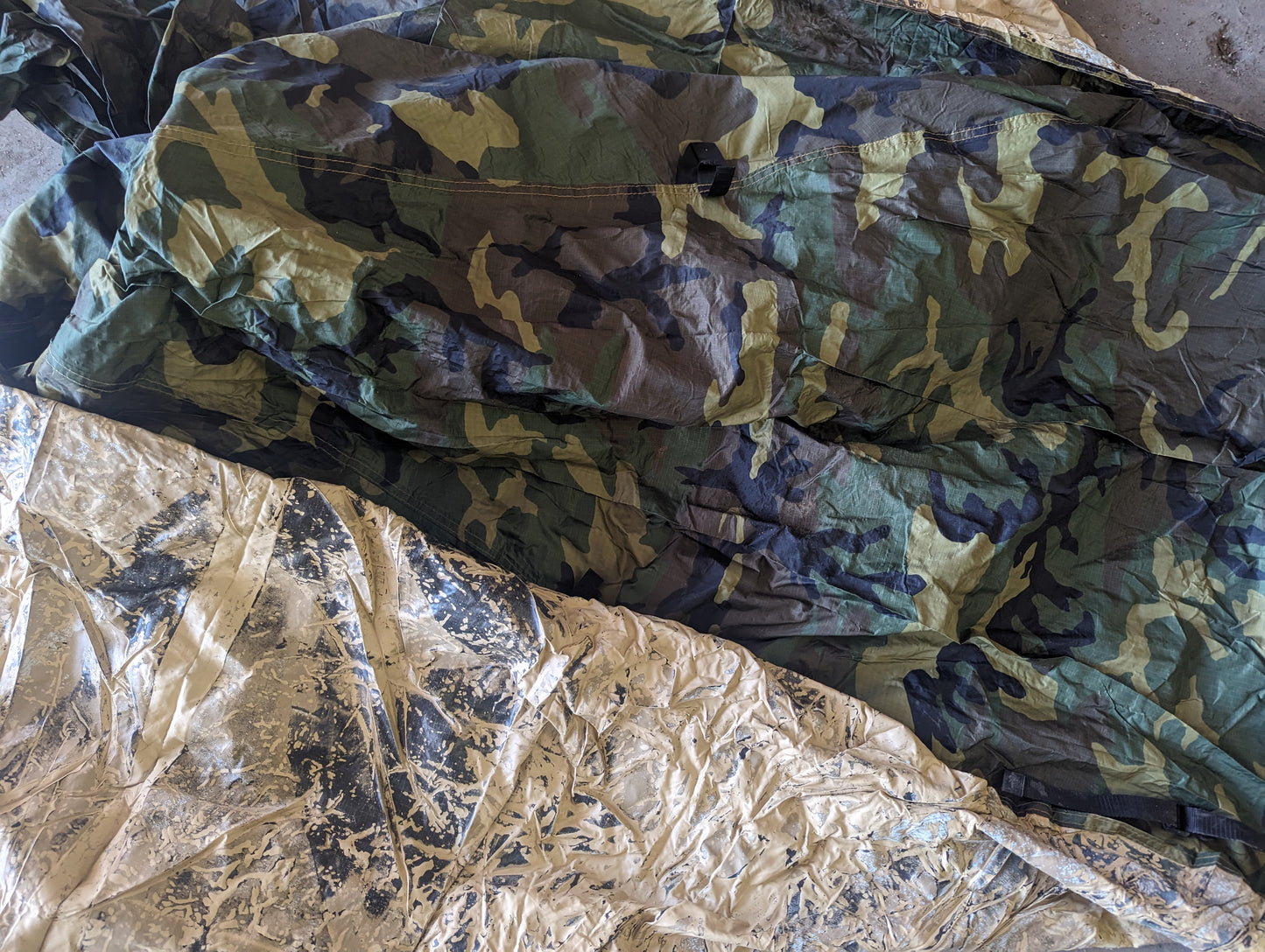 A close-up view of the interior of the U.S. Military Combat Tent (TCOP), showing the Woodland camouflage fabric and the heavily degraded, peeling silver/tan waterproof coating.