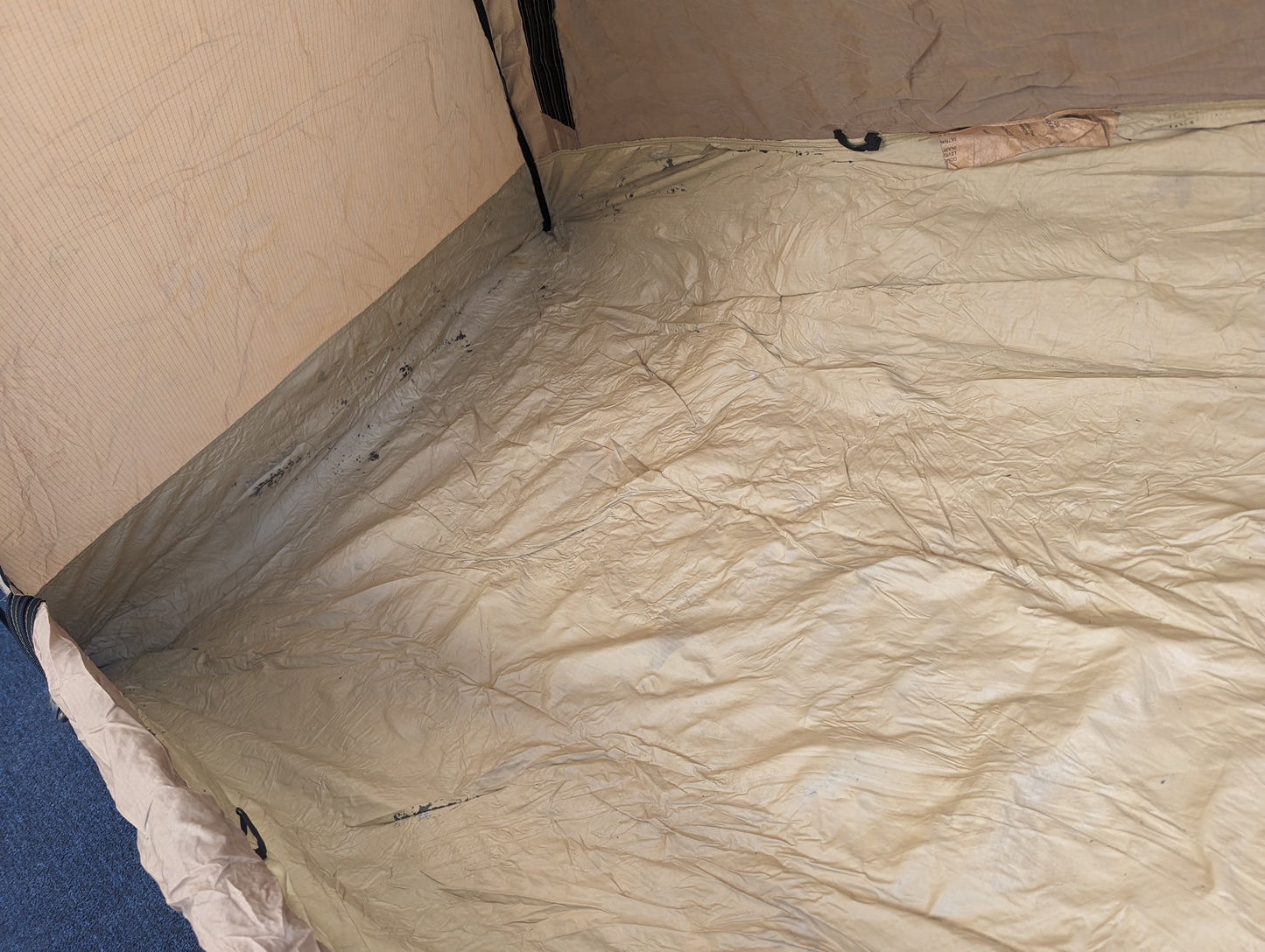 A high-angle view looking down at the interior floor of the U.S. Military Combat Tent (TCOP), displaying the wrinkled tan waterproof material and bathtub-style construction.