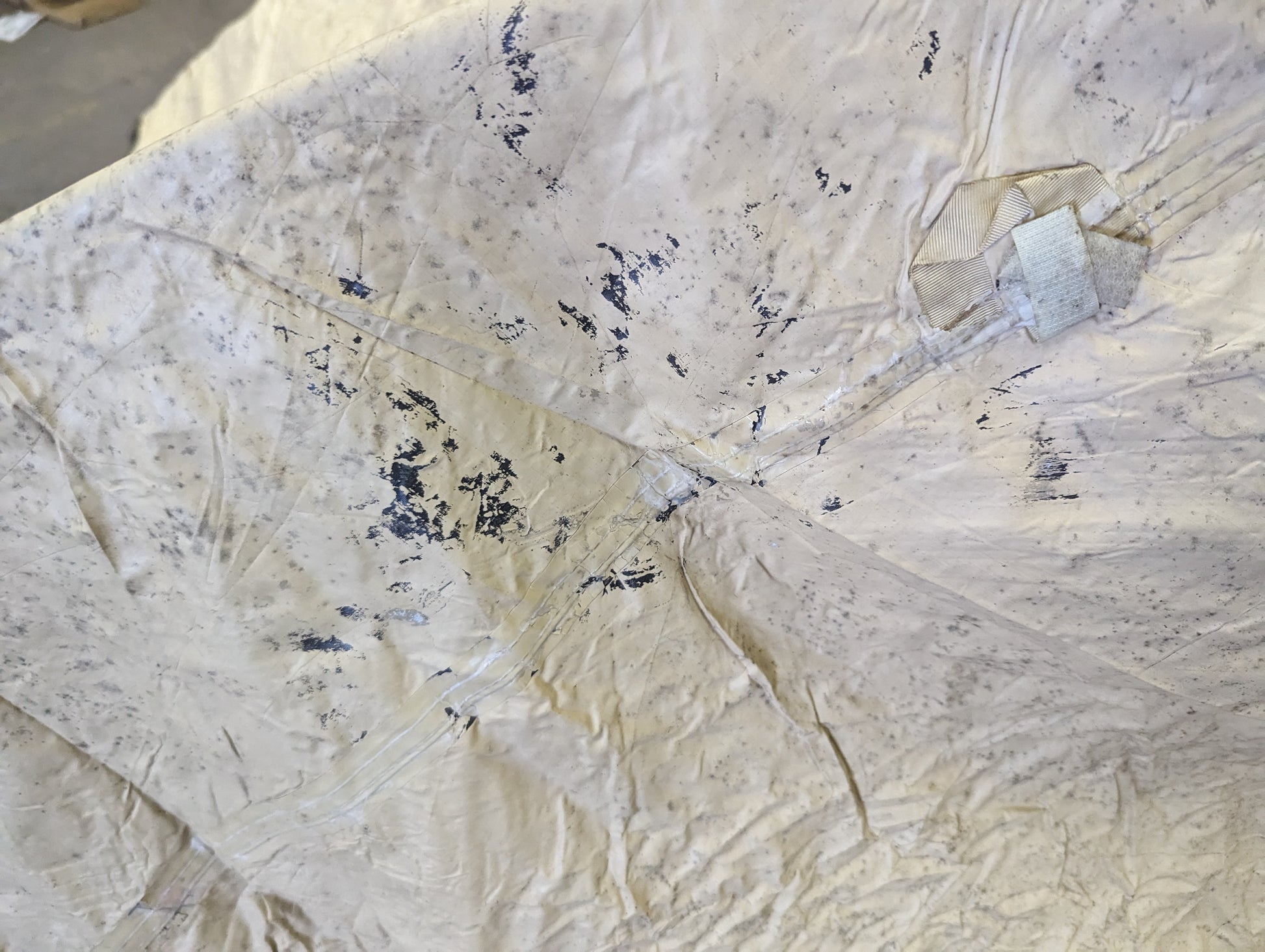 A close-up view of the interior tan coating of the U.S. Military TCOP tent rainfly, showing signs of wear such as peeling seam tape and flaking urethane coating, along with a hook-and-loop attachment strap.v