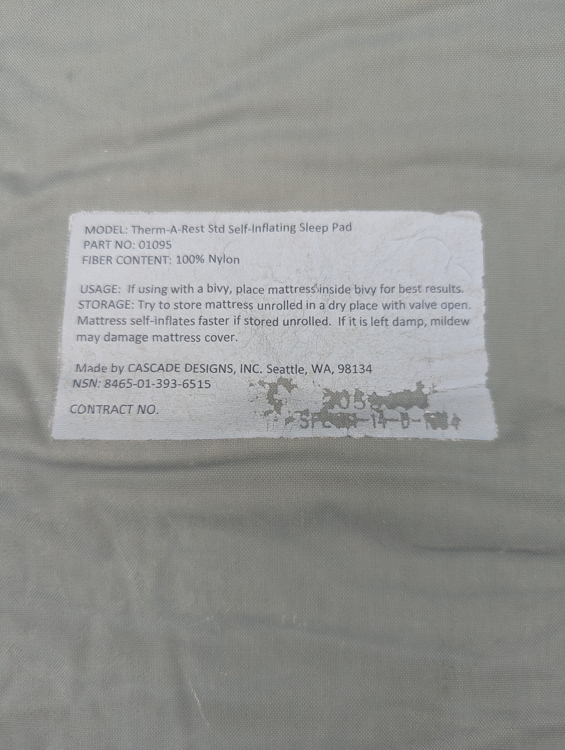 A close-up of the printed label on a U.S. Military Therm-A-Rest Standard Self-Inflating Sleep Pad, displaying usage instructions, storage care, and the National Stock Number (NSN) 8465-01-393-6515.
