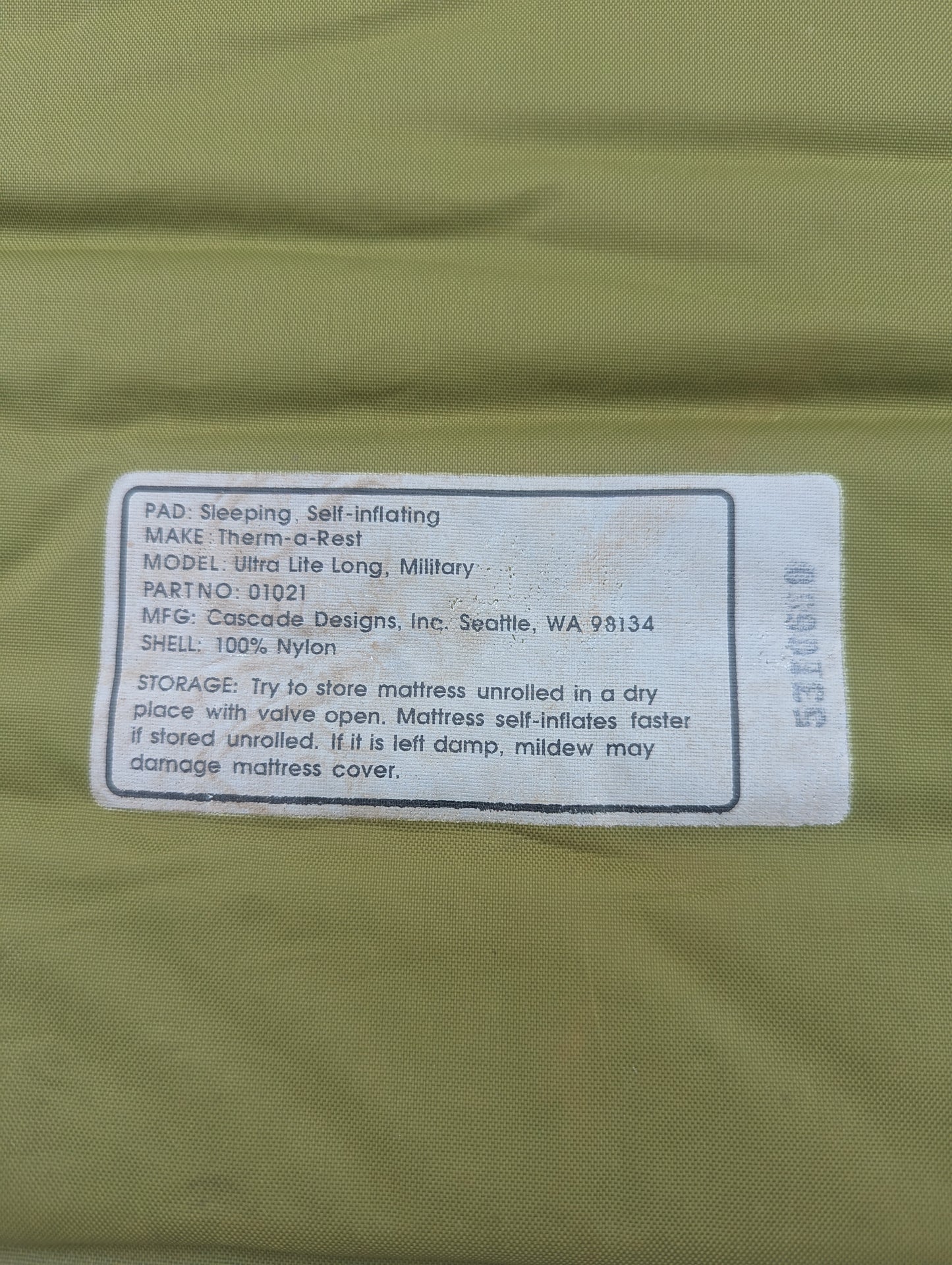 A close-up of the printed label on a U.S. Military Therm-A-Rest Ultra Lite Long self-inflating sleeping mat, displaying the model details, manufacturer Cascade Designs, and storage instructions.