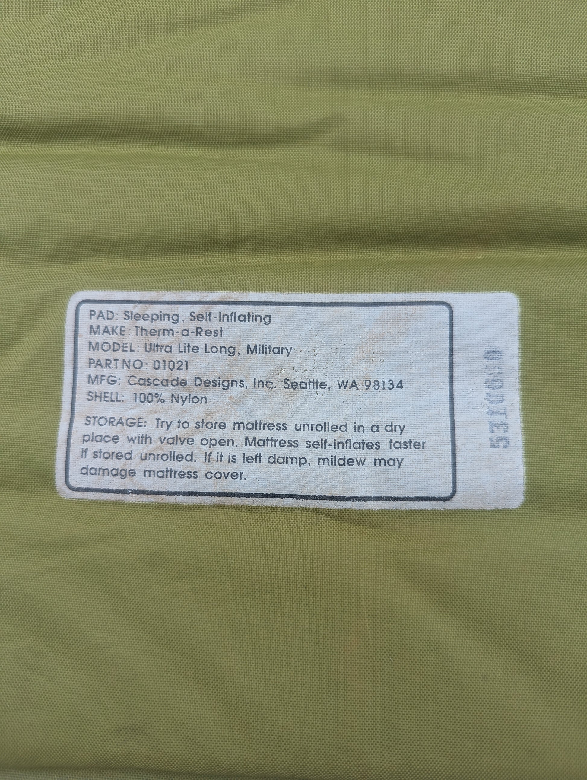 A close-up of the printed label on a U.S. Military Therm-A-Rest Ultra Lite Long self-inflating sleeping mat, displaying the model details, manufacturer Cascade Designs, and storage instructions.