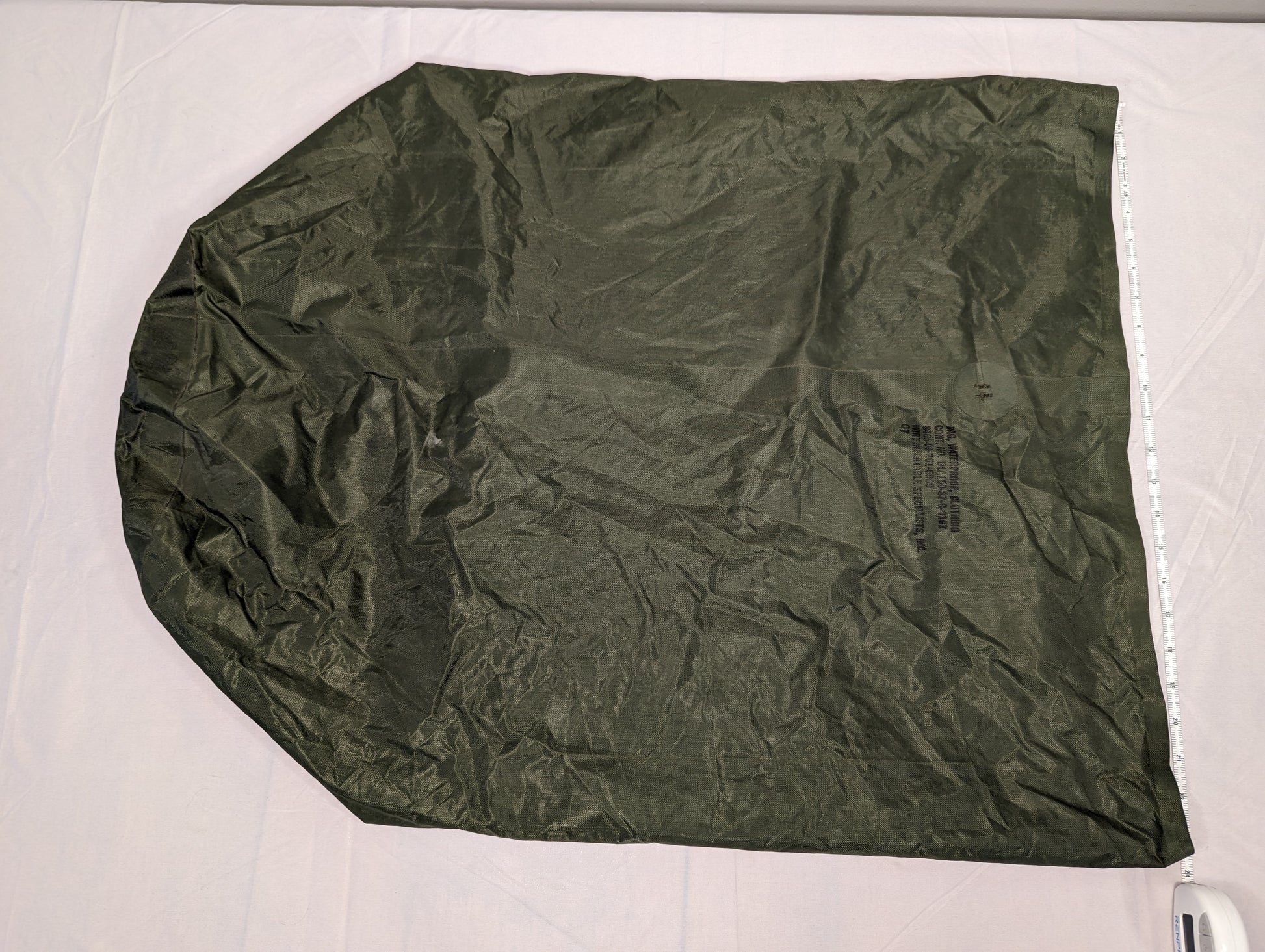 A large, fully unfolded U.S. Military Waterproof Clothing Bag in dark olive green, laid flat on a white surface, displaying its ripstop texture and large dimensions with a measuring tape along the edge.