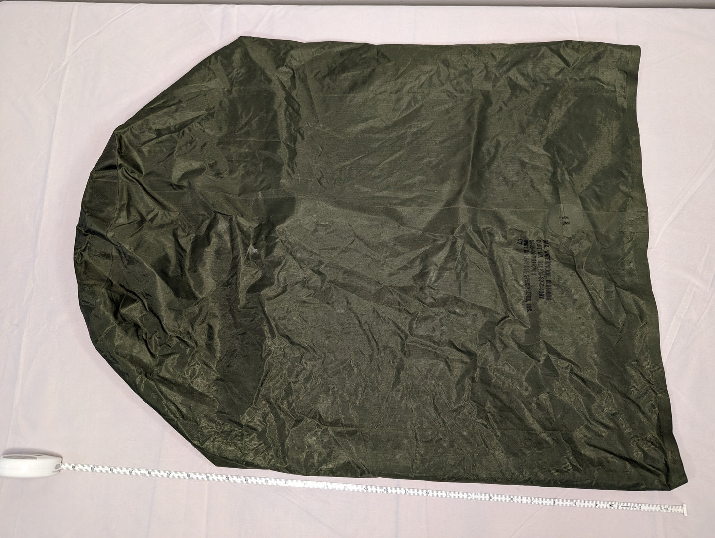 A large, fully unfolded U.S. Military Waterproof Clothing Bag in olive green ripstop nylon, laid flat on a white surface with a tape measure placed at the base to indicate the bag's dimensions.
