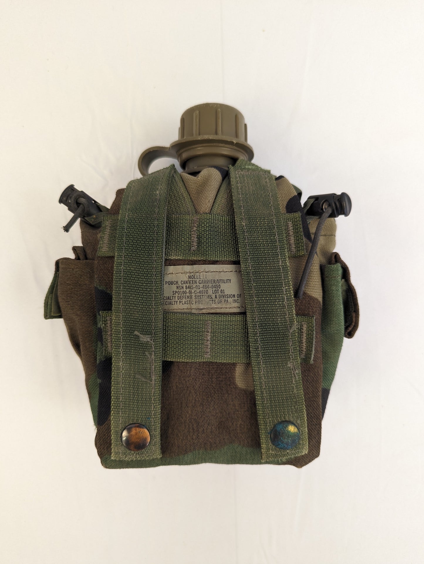 A back view of a U.S. Military Surplus Woodland camouflage 1-quart canteen pouch, displaying the vertical MOLLE attachment webbing, two drainage grommets, and the stitched manufacturer's label.