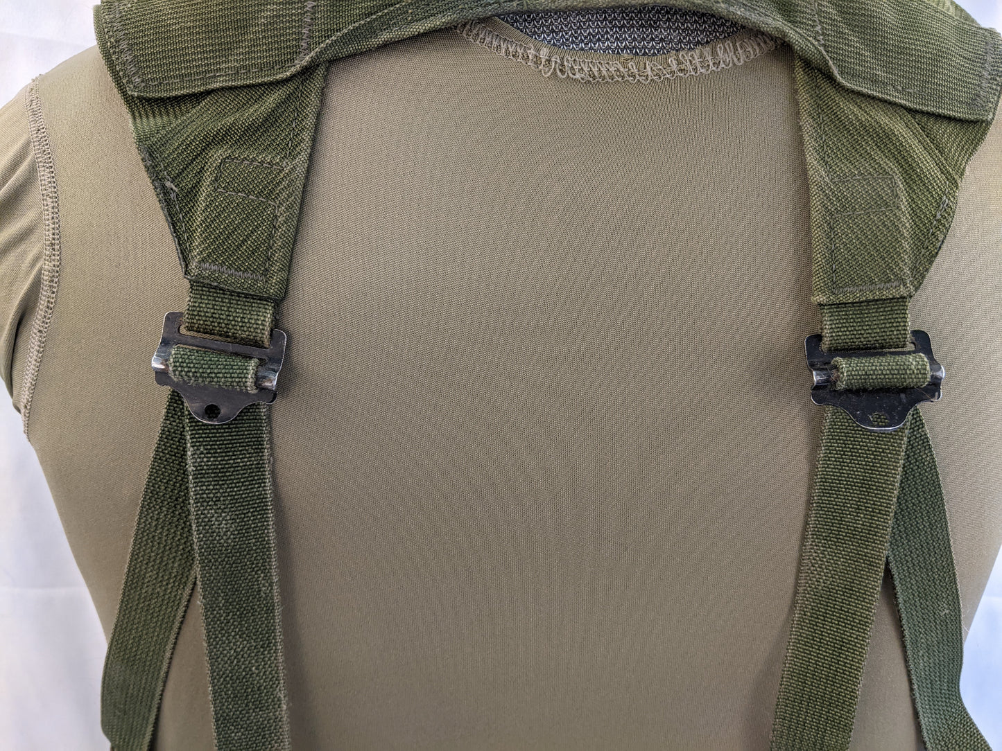 A close-up back view of a U.S. Military Fighting Load Carrier (FLC) vest in Olive Green, mounted on a mannequin, highlighting the adjustable shoulder straps and the mesh back panel.