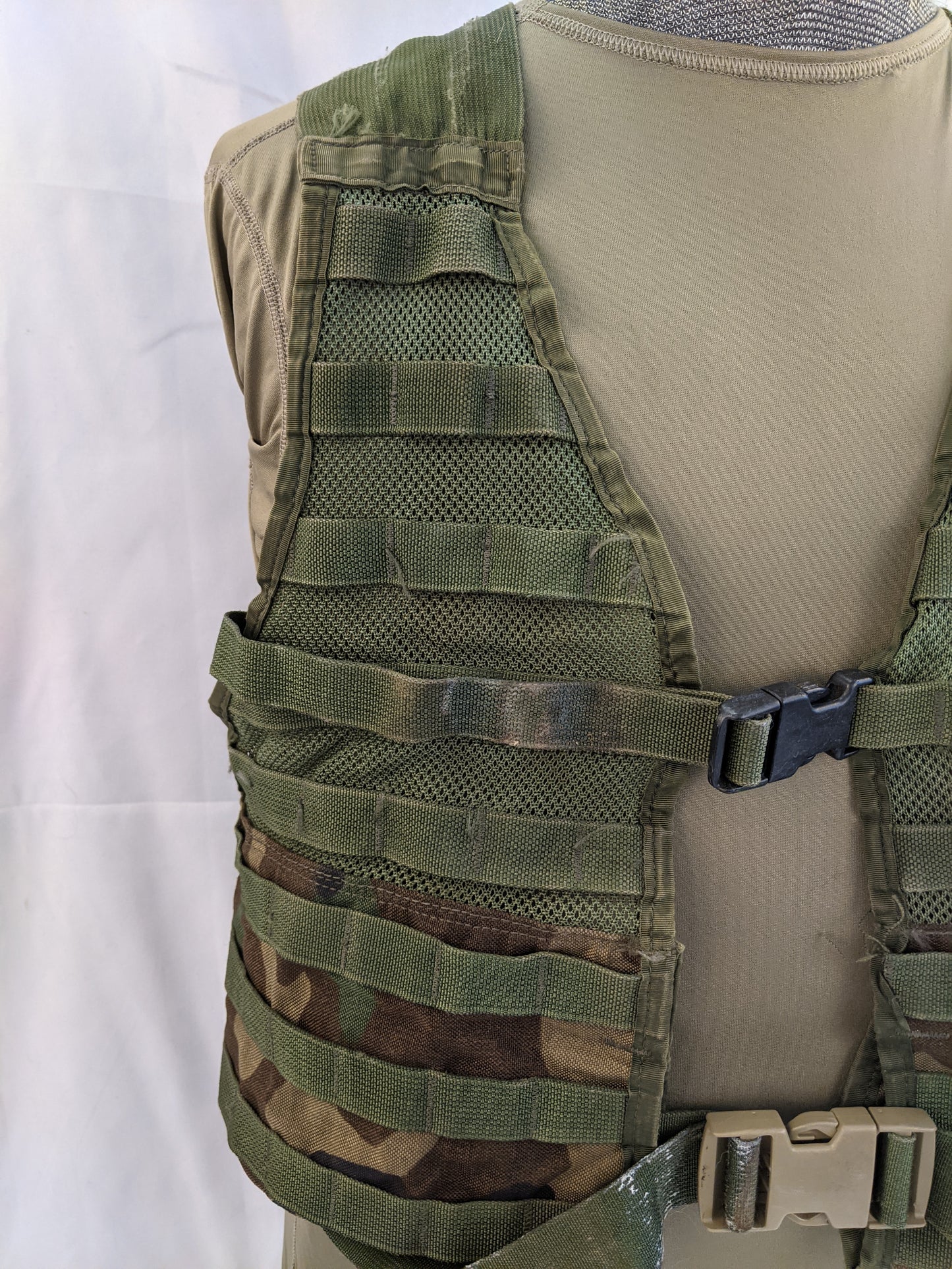 A close-up side view of the U.S. Military Fighting Load Carrier (FLC) vest in Woodland camouflage, detailing the MOLLE webbing attachment points and mesh backing on the torso panel.