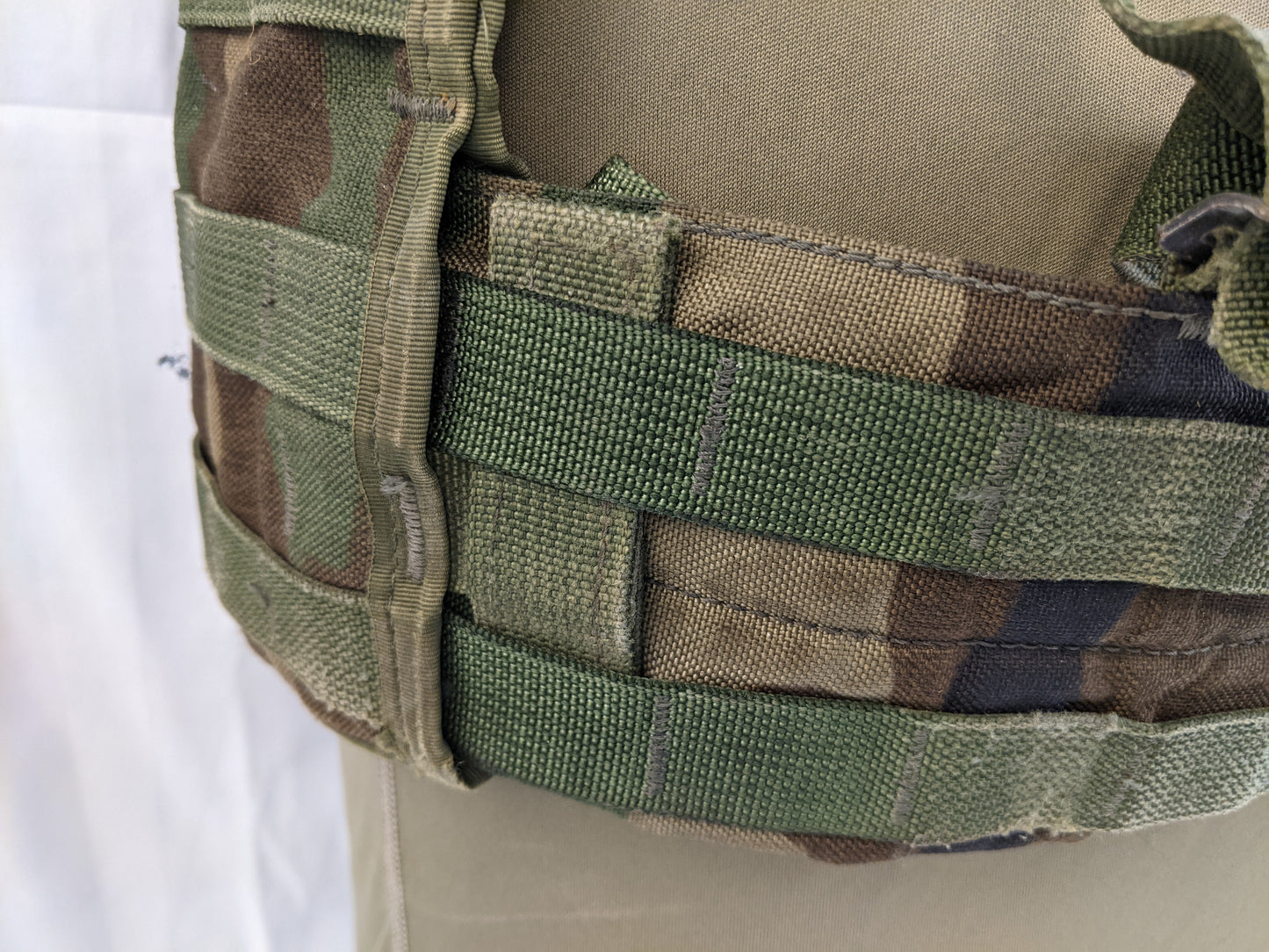 A very close-up view of the Woodland camouflage Fighting Load Carrier (FLC) vest, highlighting the three rows of dark green horizontal MOLLE webbing and the mesh backing underneath.