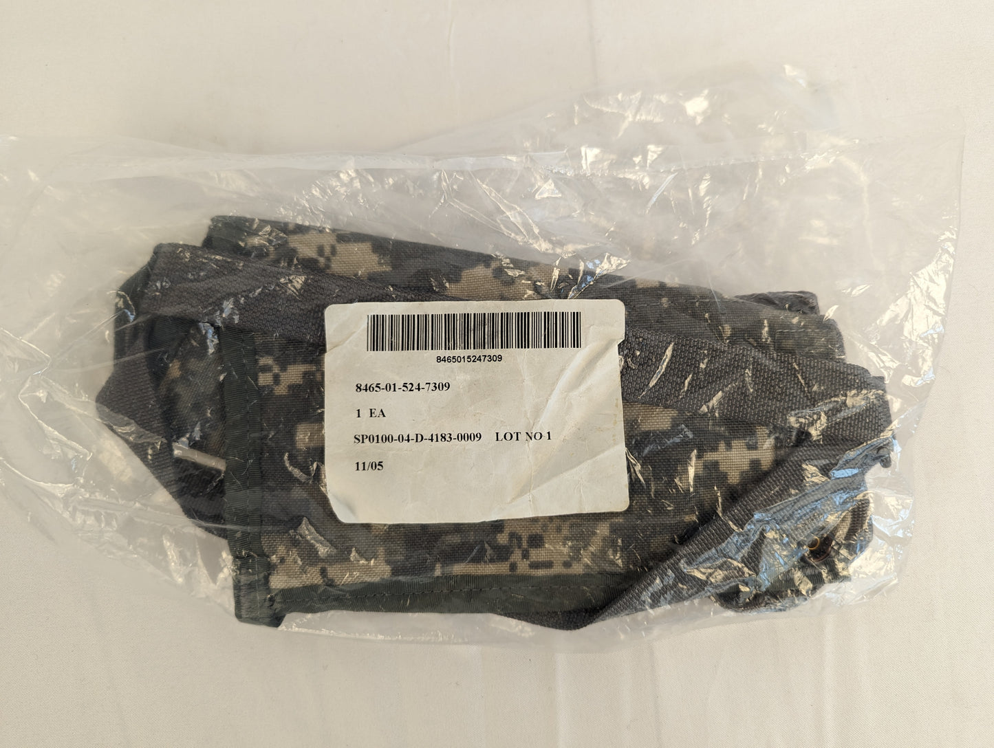 A new, sealed U.S. Military MOLLE II Bandoleer in ACU digital camouflage, packaged in clear plastic with a visible white issue label detailing the NSN and contract number.