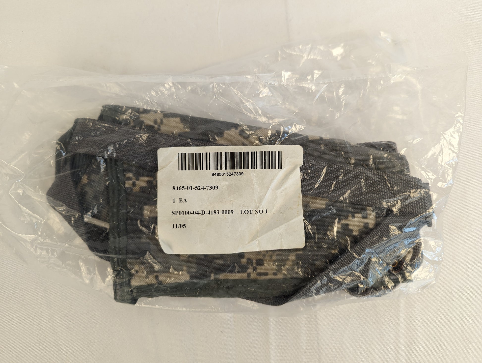 A new, sealed U.S. Military MOLLE II Bandoleer in ACU digital camouflage, packaged in clear plastic with a visible white issue label detailing the NSN and contract number.