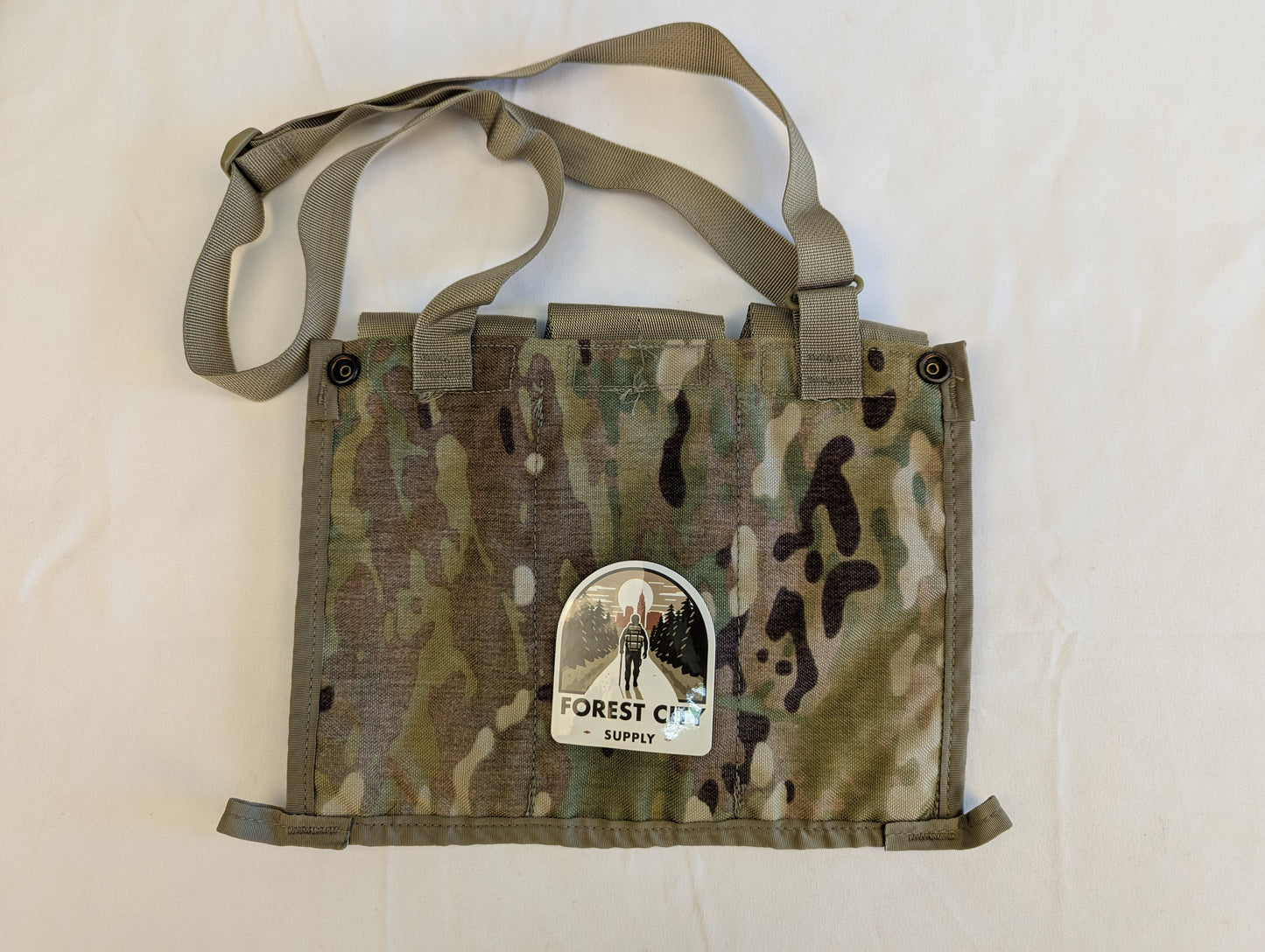 A U.S. Military Surplus OCP/Multicam Bandoleer chest rig laid flat, featuring three snap-button magazine pouches, a khaki strap, and a prominent 'FOREST CITY SUPPLY' logo sticker on the center flap.
