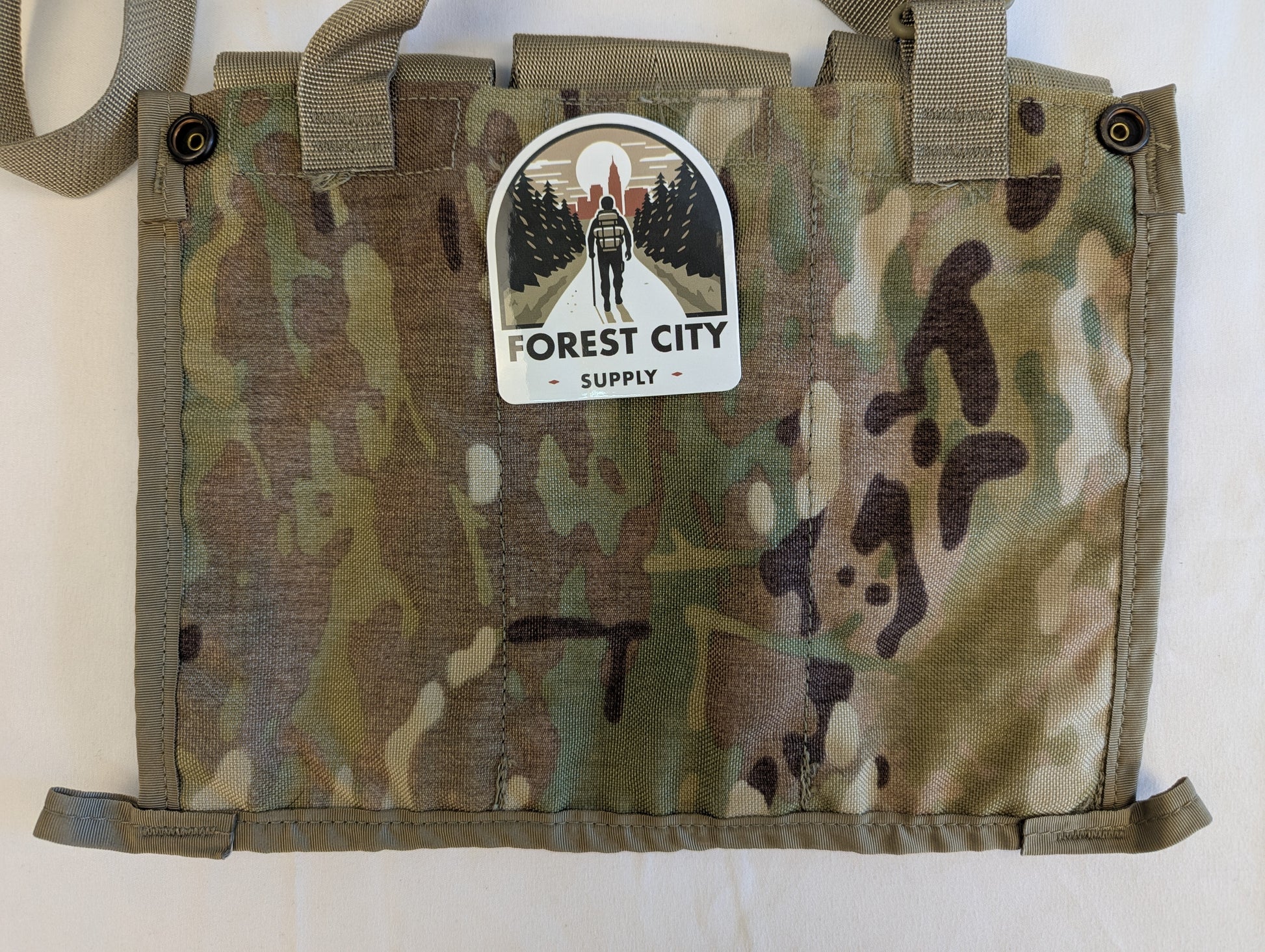 A U.S. Military Surplus OCP/Multicam Bandoleer chest rig laid flat, featuring three snap-button magazine pouches, a khaki strap, and a prominent 'FOREST CITY SUPPLY' logo sticker on the center flap.