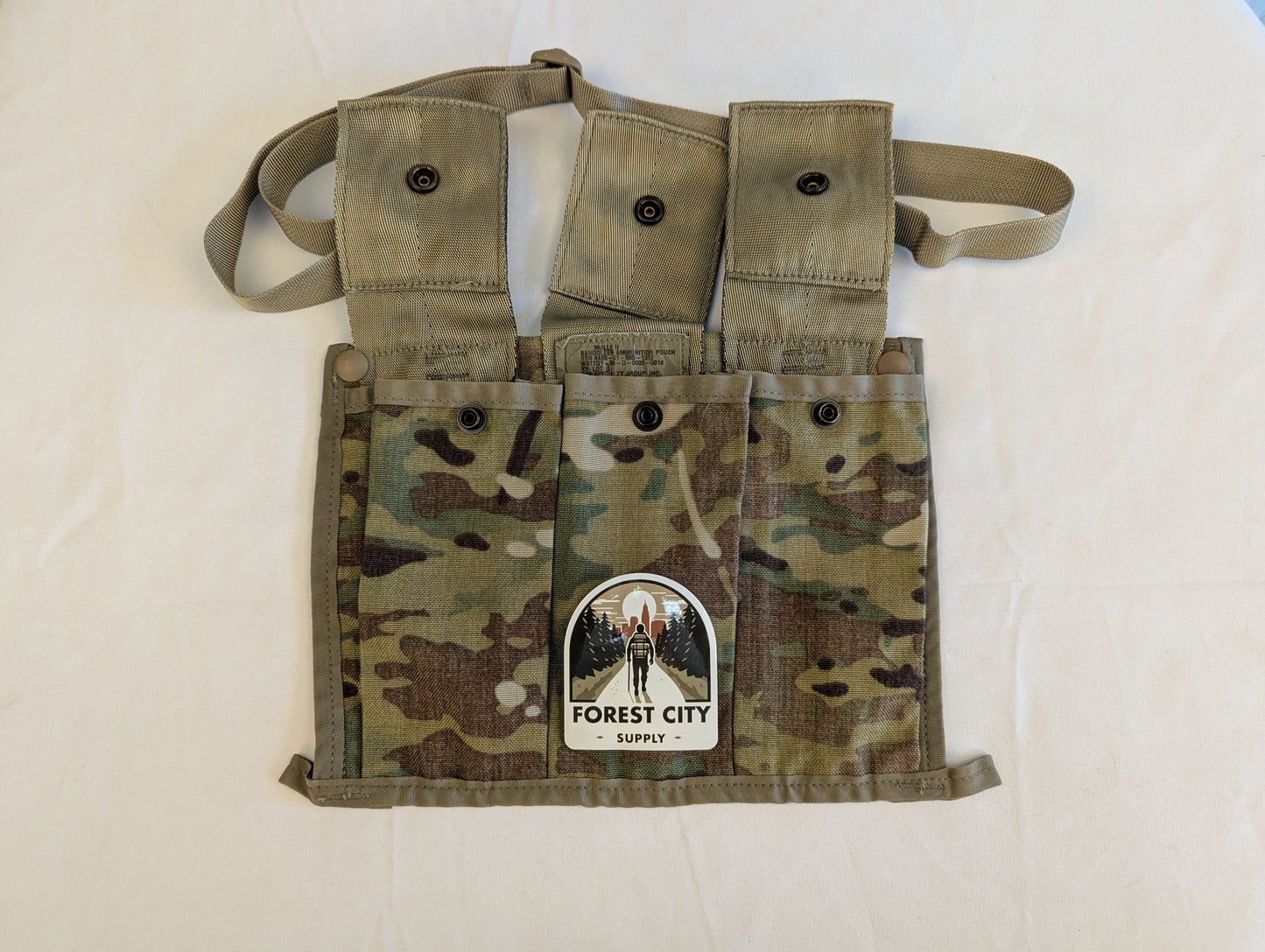A U.S. Military Surplus OCP/Multicam Bandoleer chest rig laid flat, featuring three snap-button magazine pouches, a khaki strap, and a prominent 'FOREST CITY SUPPLY' logo sticker on the center flap.