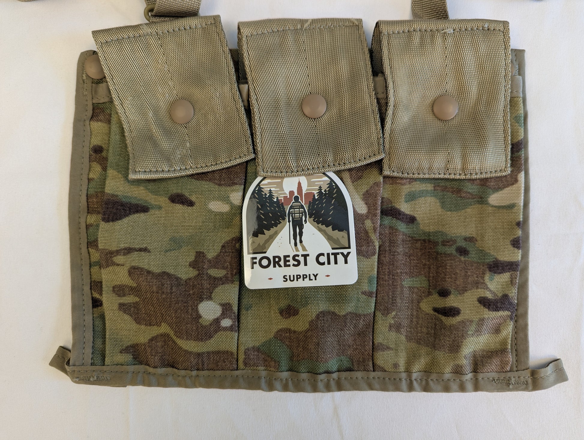 A U.S. Military Surplus OCP/Multicam Bandoleer chest rig laid flat, featuring three snap-button magazine pouches and a prominent 'FOREST CITY SUPPLY' logo sticker on the center flap.