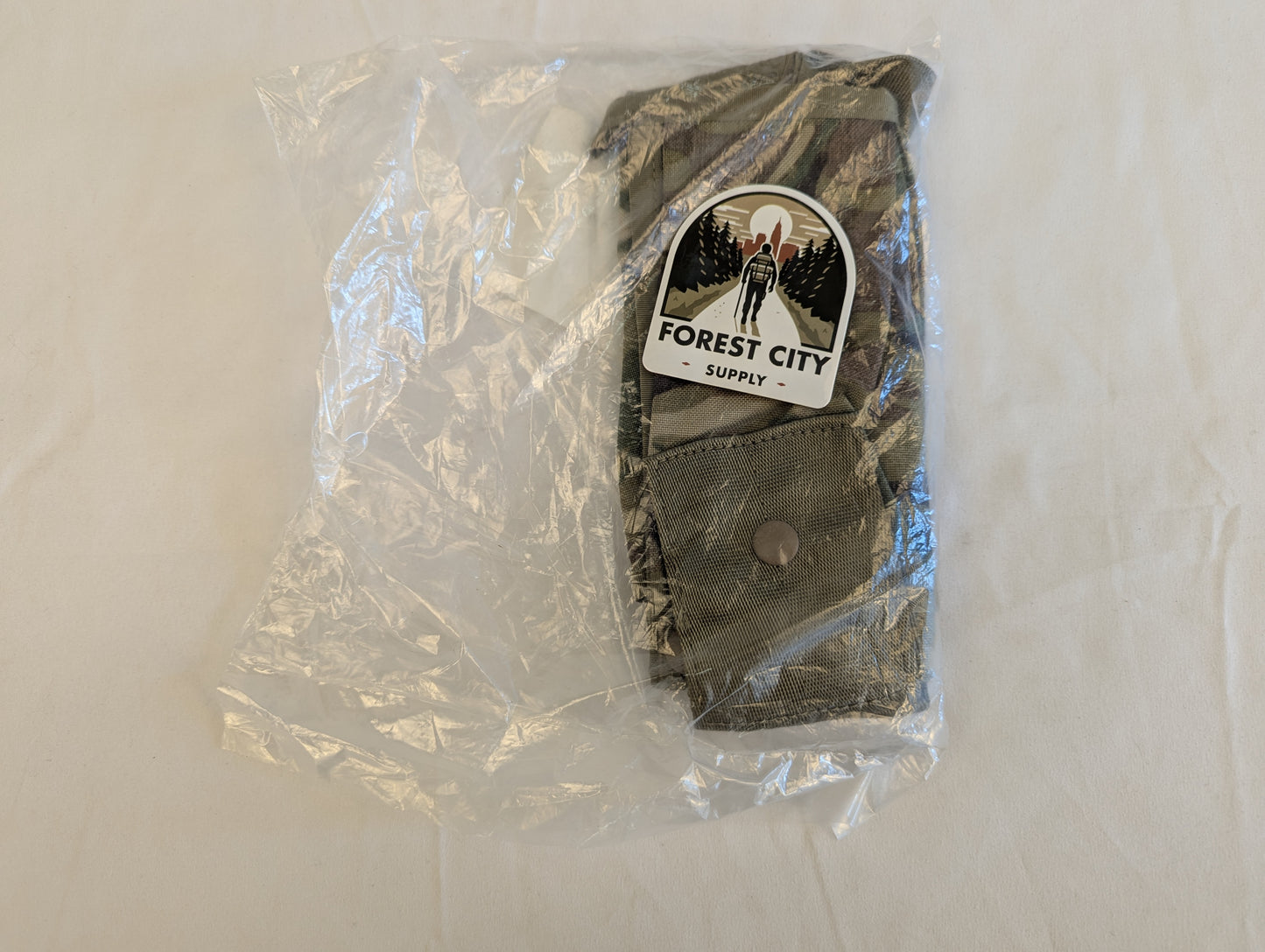 A new U.S. Military Surplus OCP/Multicam Bandoleer pouch sealed inside clear plastic packaging, with a large 'FOREST CITY SUPPLY' logo sticker covering the front.