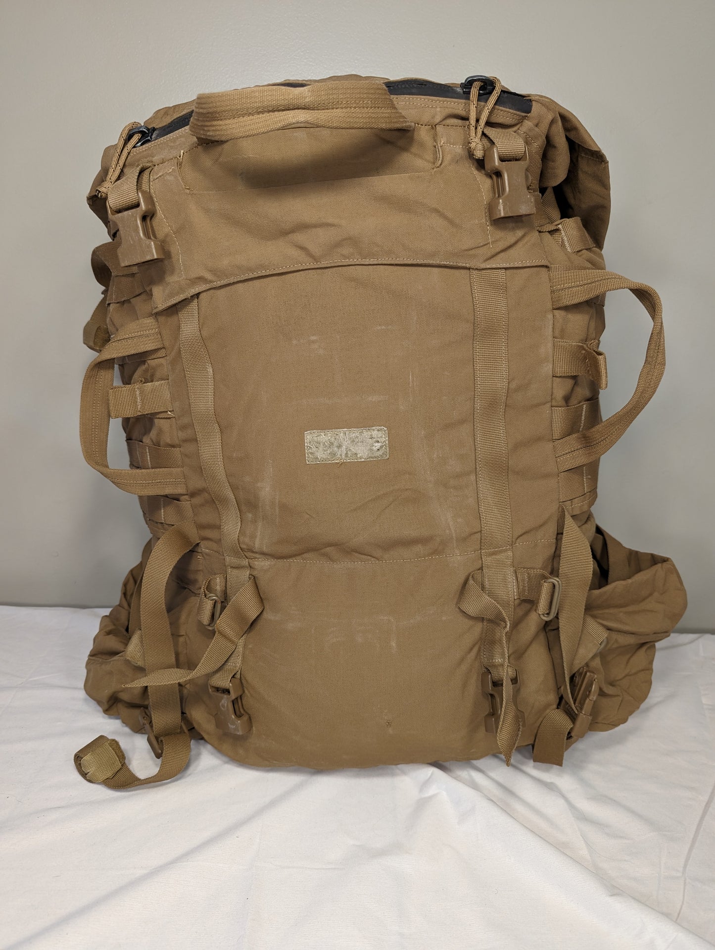 A large U.S. Military Surplus USMC FILBE Main Field Pack in Coyote Brown, photographed from the front, showing numerous compression straps, MOLLE webbing, and a center identification patch field.