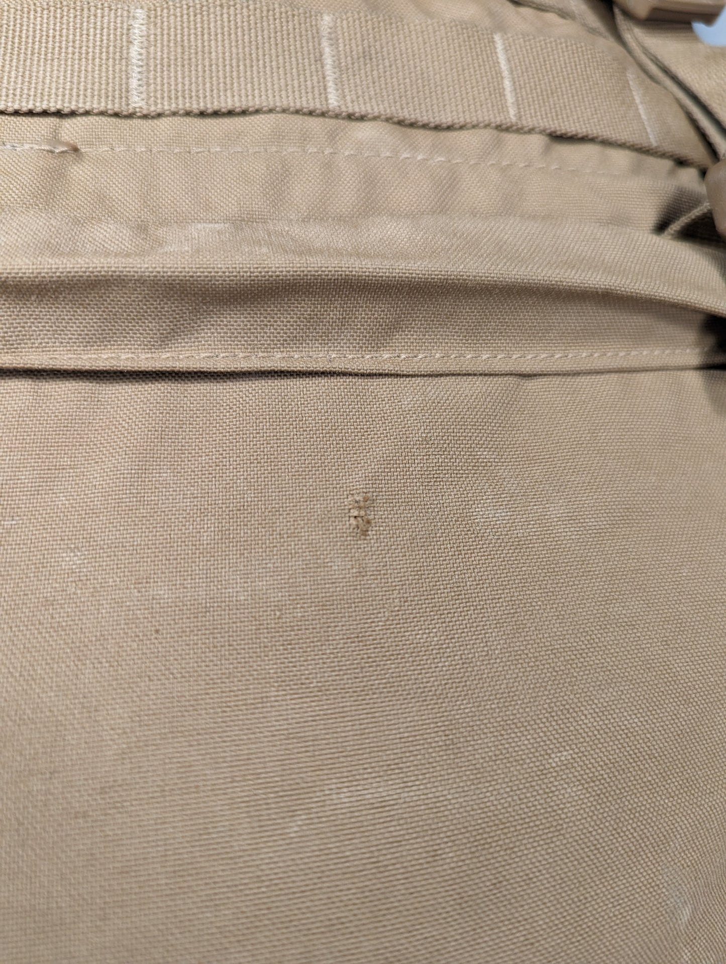 A close-up detail shot of the Coyote Brown fabric on a USMC FILBE Rucksack, showing a small dark stain or spot on the exterior material, indicating surplus condition.