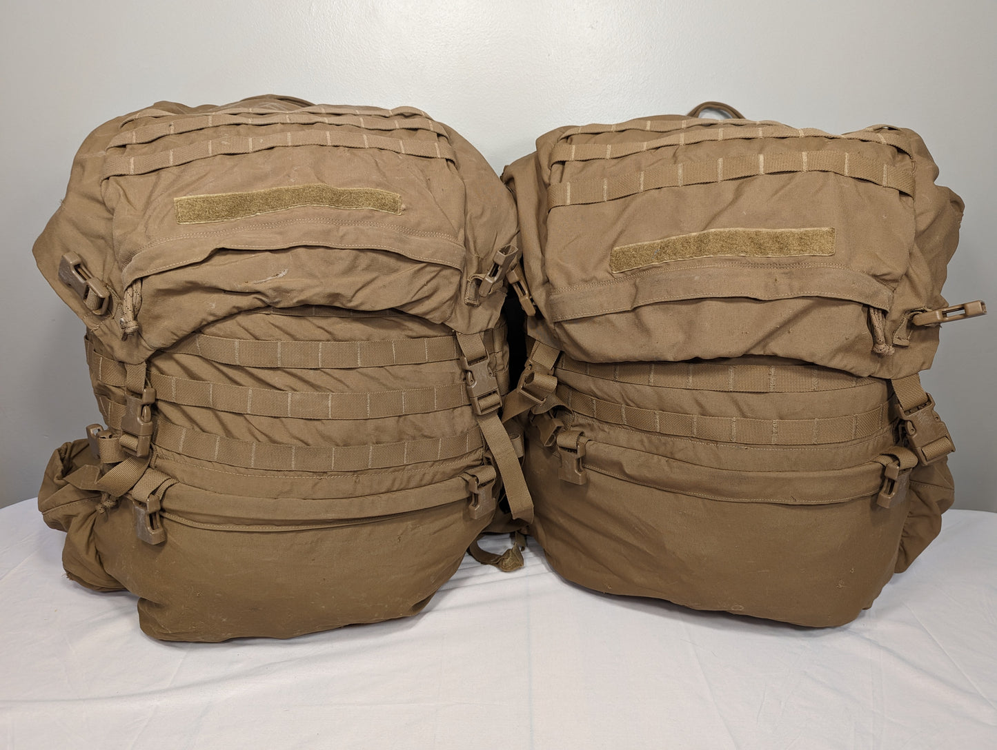 Two U.S. Military Surplus USMC FILBE Rucksacks in Coyote Brown displayed side-by-side on a white background, featuring extensive MOLLE webbing, adjustable compression straps, and hook-and-loop fields on the top flaps.