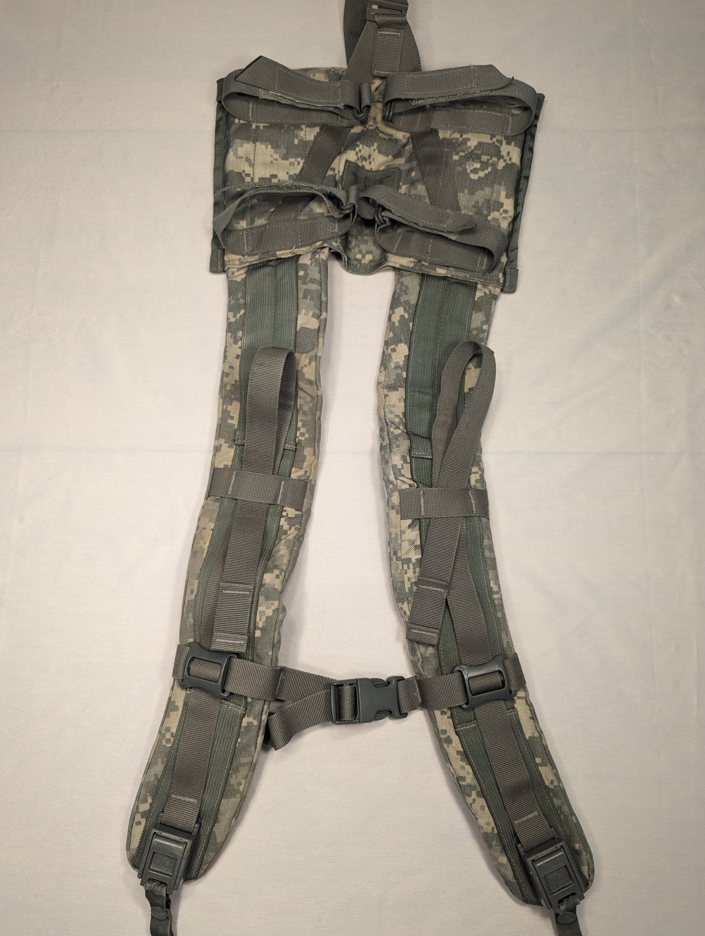 A close-up view of a U.S. Military Surplus Enhanced Frame Shoulder Straps assembly in ACU digital camouflage, laid flat, showing the padded construction, top yoke, and black plastic adjustment buckles.